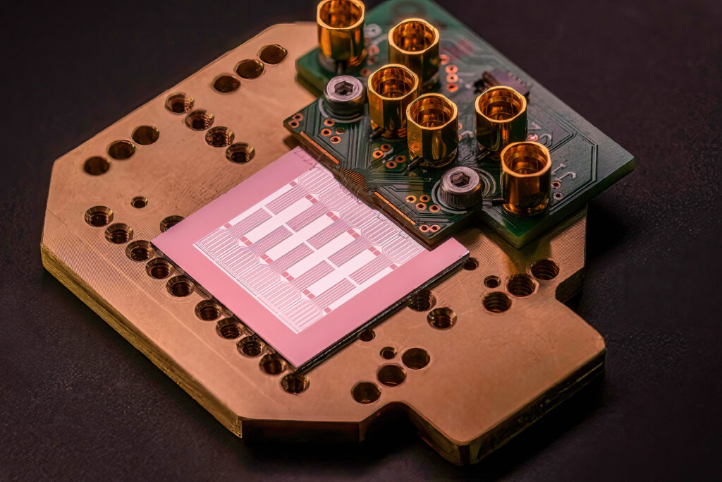 A close up image of Photonic’s photonically linked silicon spin qubit chip with copper and gold components on a black background.